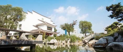 A traditional building with a reflection in the water, a stone bridge, and trees.