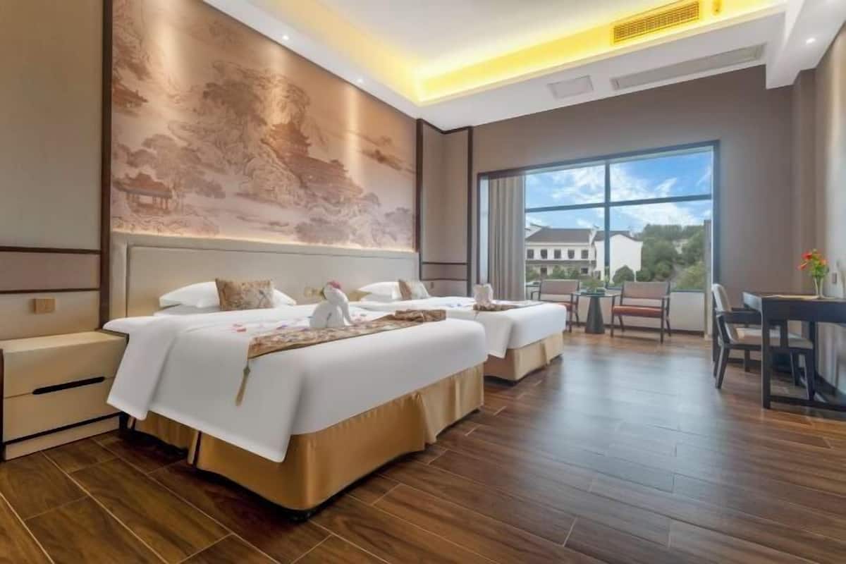 Habitación de hotel con dos camas, zona de comedor y un ventanal con vistas.
