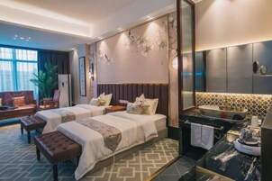 Quarto de hotel com duas camas, um sofá, uma janela ampla, um espelho, uma pia e uma planta.