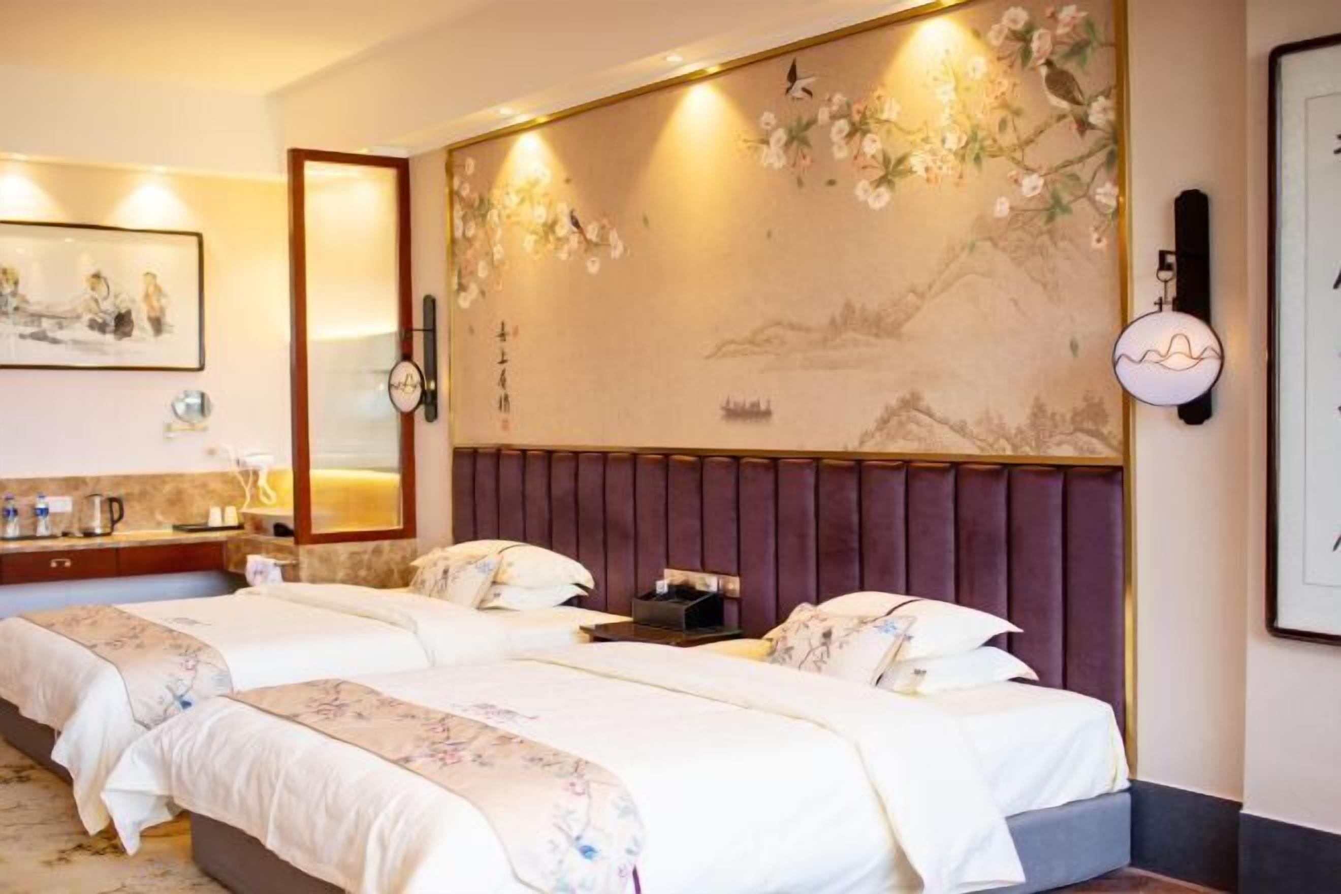 Quarto de hotel com duas camas, um grande mural na parede, cabeceira de madeira, mesa de cabeceira e luminária fixa na parede.