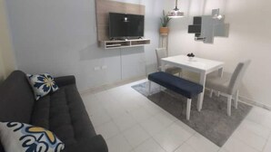 En moderne stue med sofa, spisebord og stole. Der er et fladskærms-tv monteret på væggen.