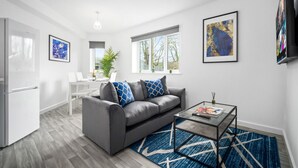 Ein modernes Wohnzimmer mit einem grauen Sofa, einem Glastisch und einem blau gemusterten Teppich.