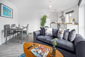 Ein modernes Wohnzimmer mit einem grauen Sofa, einem Holztisch mit einer Zeitschrift, einer Fernbedienung und einer Pflanze.