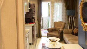 A compact living space with a kitchenette, a sofa, a coffee table, and a floor lamp. - ŞİRİNYER ELİT RESİDANCE APART HOTEL (Izmir)