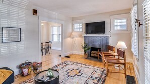 Ein Wohnzimmer mit Kamin, einem darüber montierten Fernseher und einem Essbereich mit Stühlen und einem Tisch.