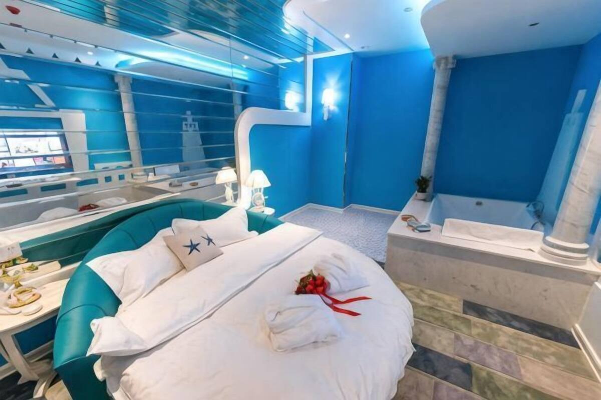 A modern hotel room with a large bed, a bathtub, and a dining area.