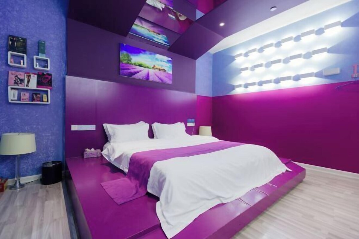 A modern bedroom with a bed, purple walls, and a ceiling with recessed lighting.