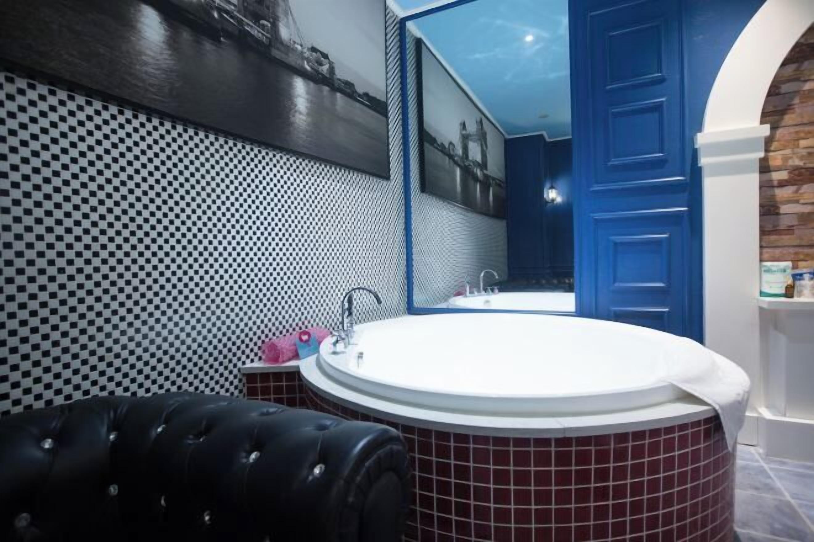 Een badkamer met een rond ligbad, een zwarte lederen fauteuil, een wastafel en een blauwe deur.