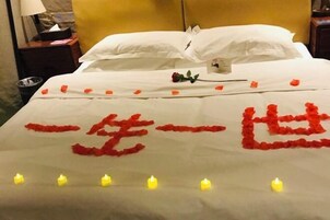A bed with rose petals and candles, a white pillow, and a yellow headboard.