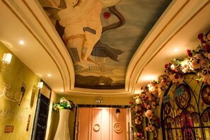 Et hotellobby med et dekorativt loft, en receptionsdisk og blomsterarrangementer.