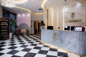 Et hotellets receptionsområde med et ternet gulv, en marmorstående disk og et skilt med et krone-emblem.