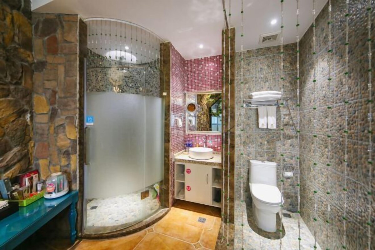 A bathroom with a stone wall, a glass shower enclosure, a sink with a mirror, and a toilet.