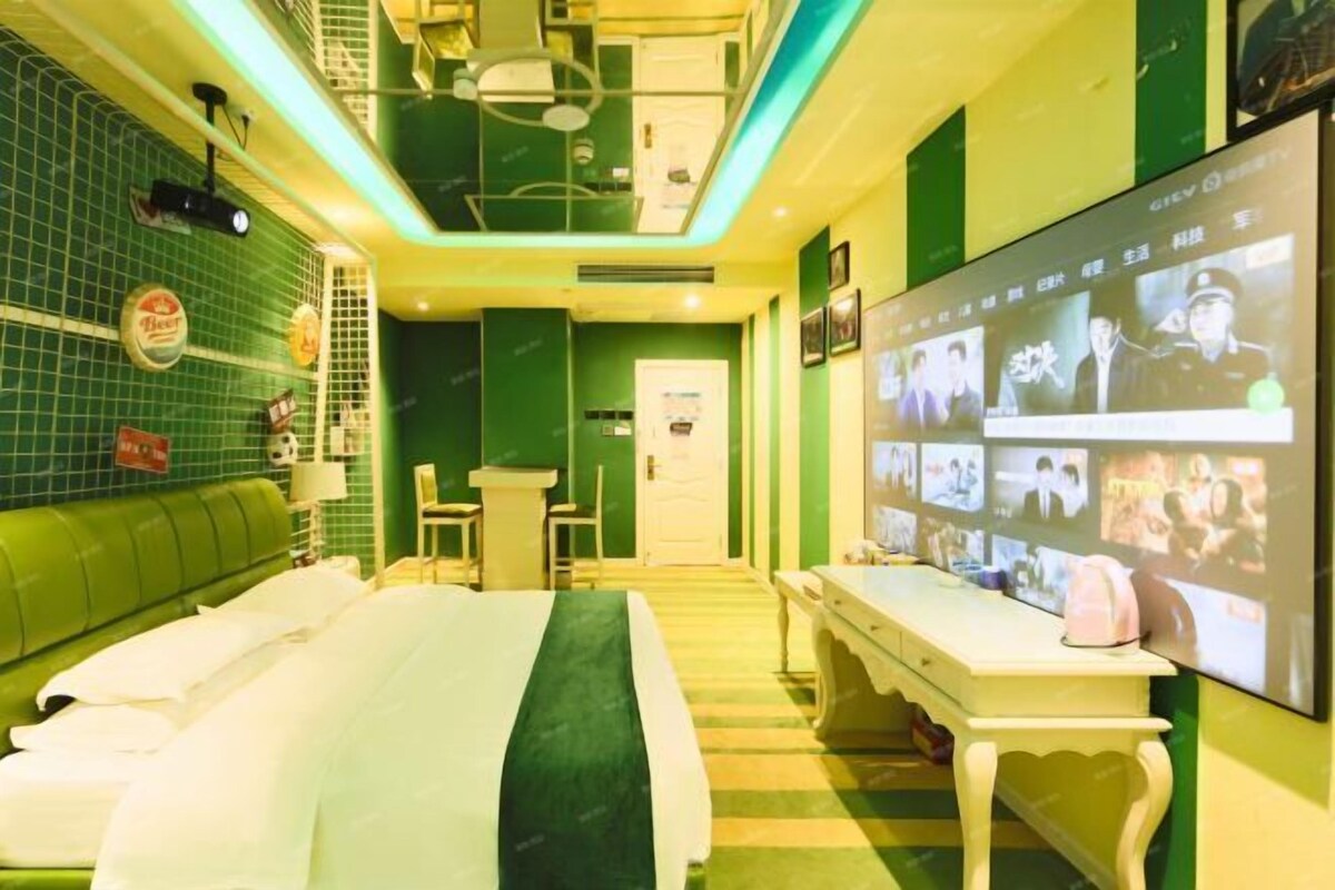 A hotel room with a bed, a desk, a chair, a television, and a green wall.