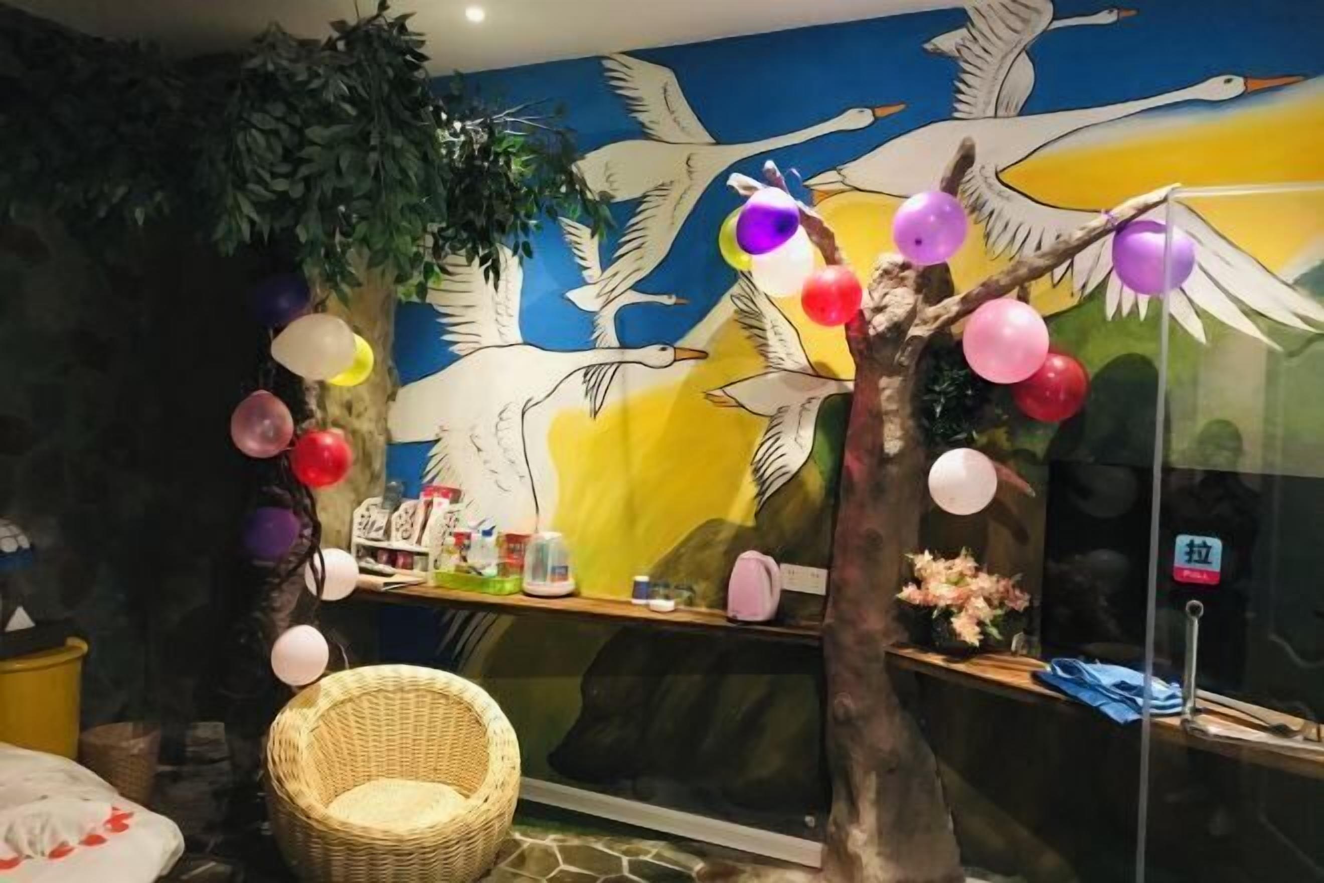 A room with a mural of birds, a wicker chair, and a shelf with various items.