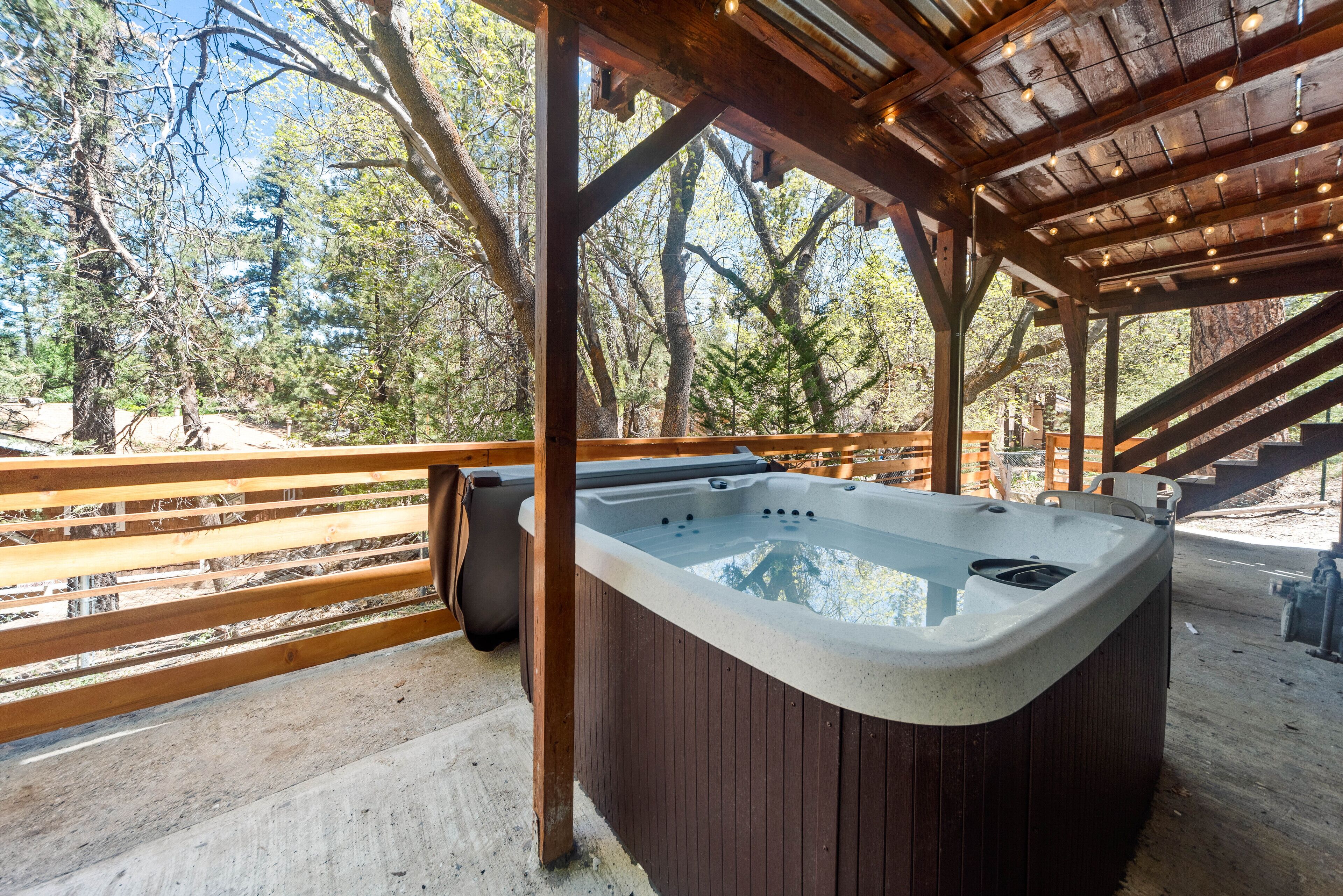 A hot tub under a wooden pergola with a view of trees.