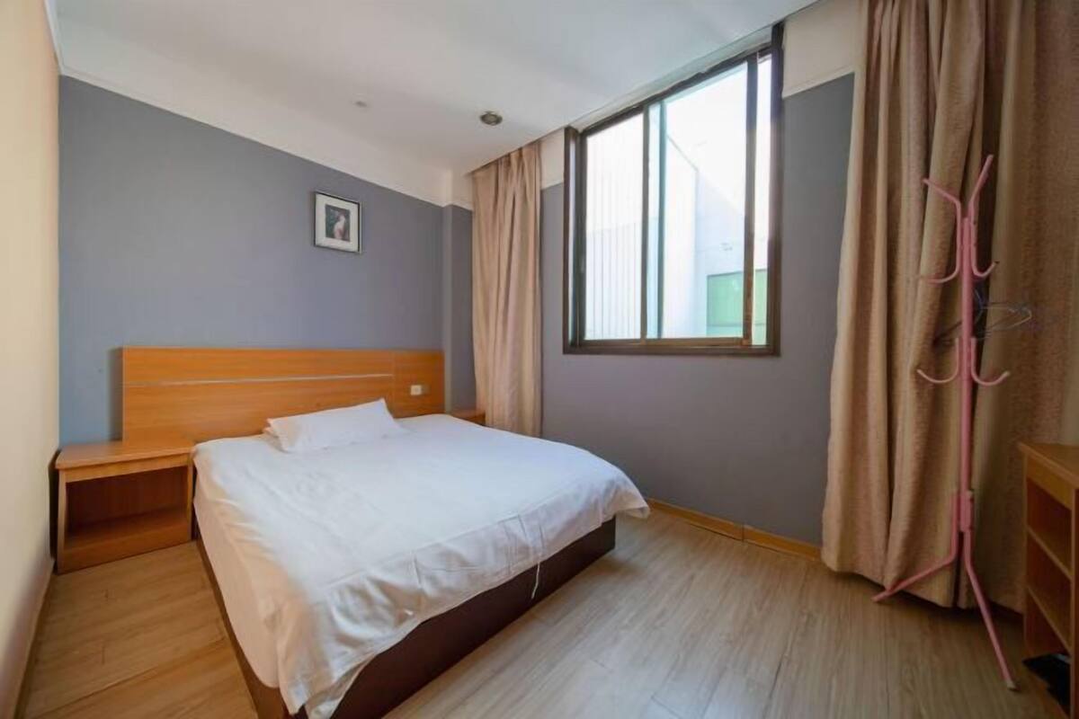 A bedroom with a wooden bed, a nightstand, a window with curtains, and a wall-mounted coat rack.