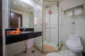 Un baño con cabina de ducha de vidrio, inodoro blanco y encimera negra con espejo.