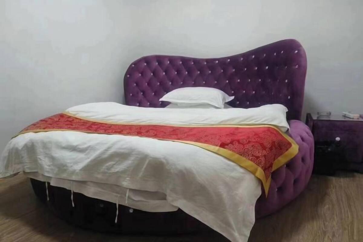 A bed with a purple headboard and a white and red bedspread.