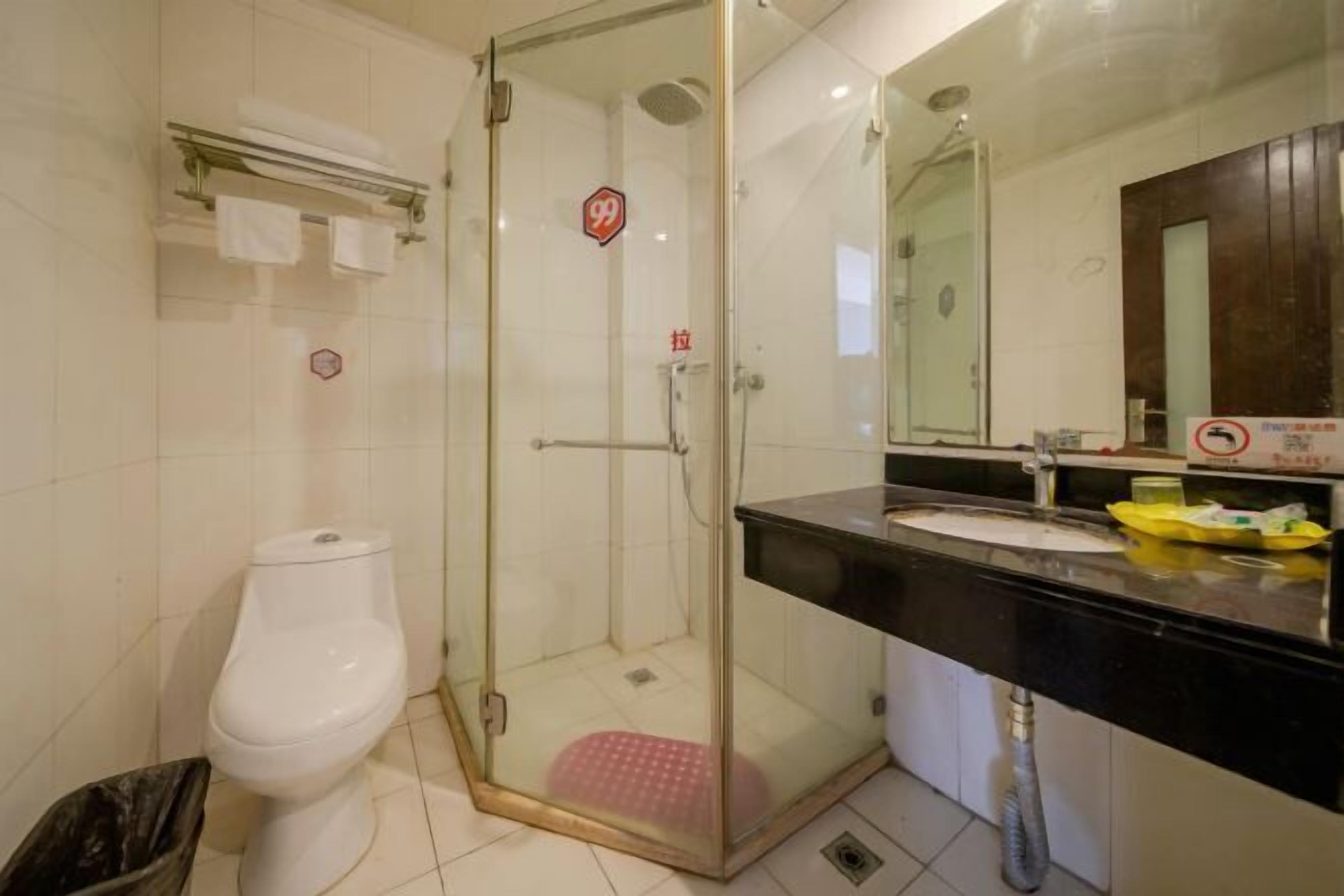 A bathroom with a glass-enclosed shower, a toilet, a sink with a mirror, and a trash bin.