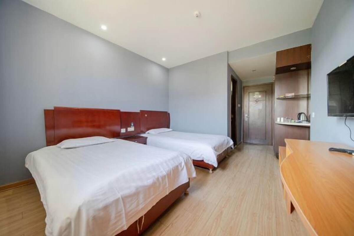 A hotel room with two beds, a wooden desk, a television, and a kitchenette.
