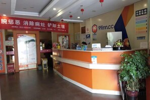 A reception area with a counter, a potted plant, and a wall with a logo and text. - 99 Inn Chain (Changshu Fangtayan Baibaiban) (Changshu)