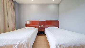 Habitación de hotel con dos camas individuales, cabeceros de madera, una mesita de noche con lámpara y suelo de madera.