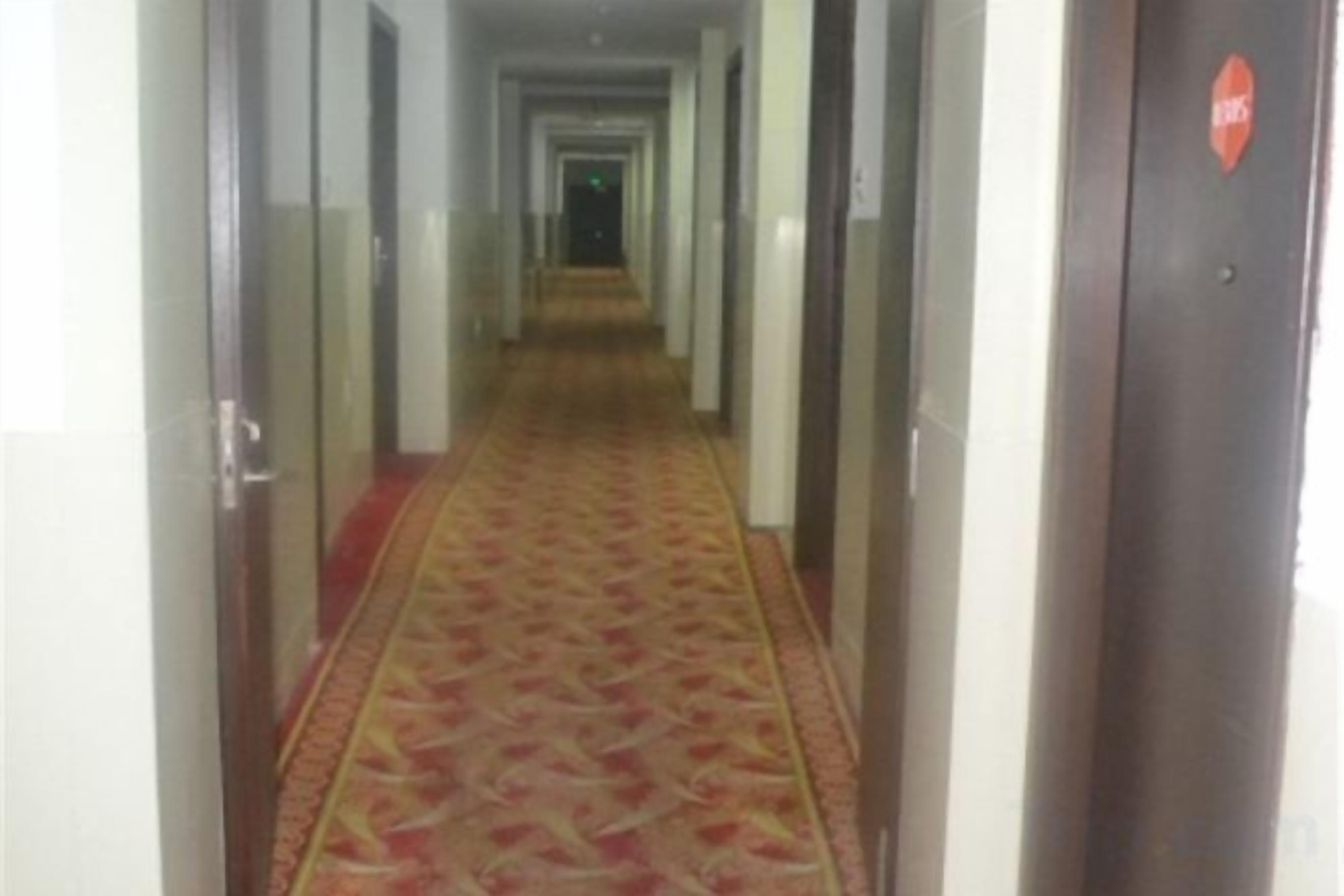 A hotel corridor with a patterned carpet, doors on both sides, and a door with a red sign on the right.