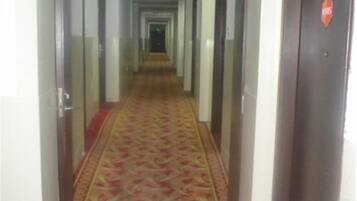 A hotel corridor with a patterned carpet, doors on both sides, and a door with a red sign on the right.