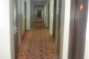 Un pasillo de hotel con alfombra estampada, puertas a ambos lados y una puerta con un cartel rojo a la derecha.
