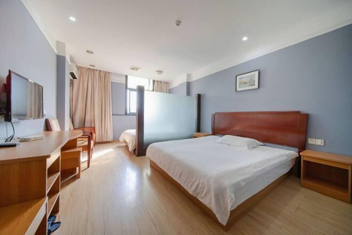 A hotel room with a bed, a desk, a chair, a TV, and a window with curtains.