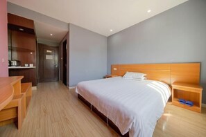 A hotel room with a bed, wooden nightstands, a desk, and a kitchenette.