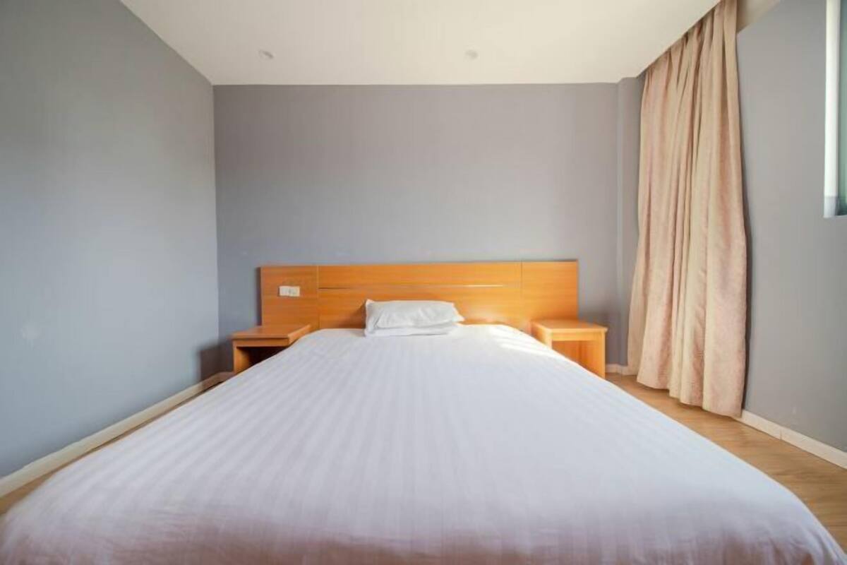 A bedroom with a wooden headboard, a single bed, two bedside tables, and a window with curtains.