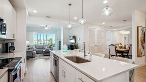 A modern kitchen with a large island, white cabinetry, and pendant lighting. - Harbor Condos 305 - Brand new, steps to beach w/pool! (Madeira Beach)