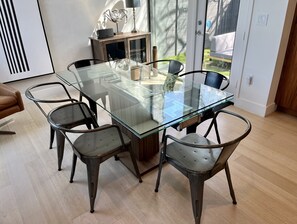A modern dining area with a glass-top table surrounded by metal chairs, a wooden cabinet with decorative items, and a view of the outdoors through a glass door. - Heated Pool Oasis, Walkable Prime Location, Skyline Views, Chefs Kitchen (Austin)