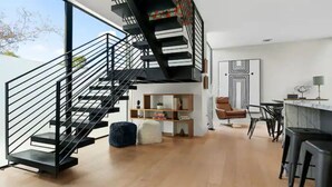 Un intérieur moderne avec un escalier noir, un plancher en bois, une bibliothèque, un fauteuil en cuir marron et un coin bar.