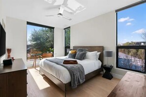 A modern bedroom with a large bed, a desk, and a window with a view of trees and buildings. - Heated Pool Oasis, Walkable Prime Location, Skyline Views, Chefs Kitchen (Austin)