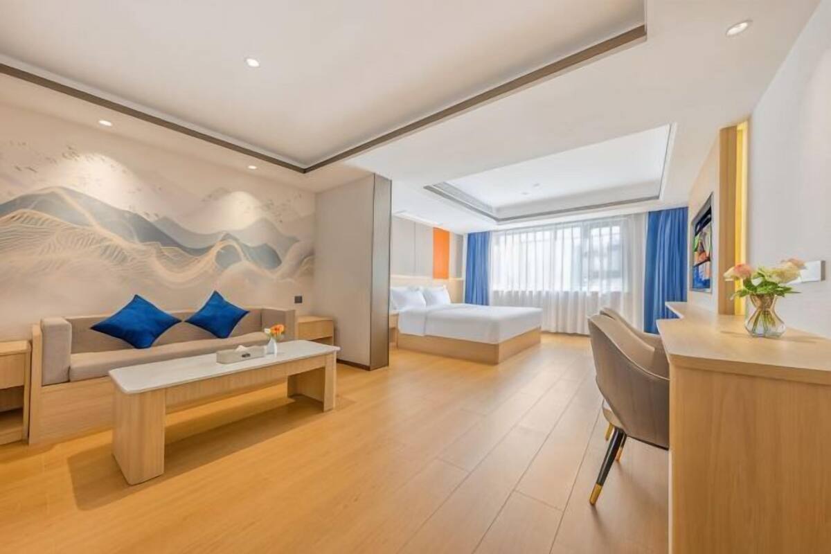 A modern hotel room with a sofa, a coffee table, a desk, and a bed.