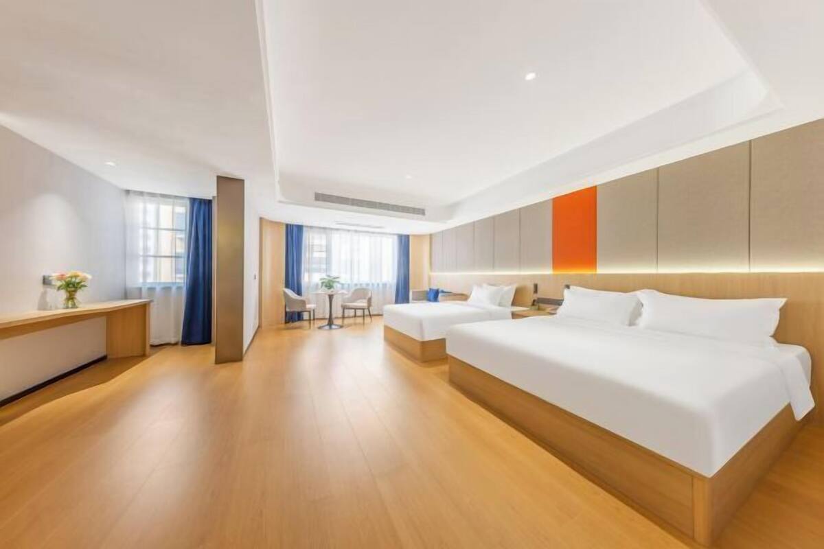 A modern hotel room with two beds, a desk, and a small seating area.