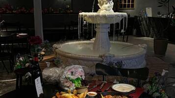 A dining area with a fountain centerpiece, tables set with plates and glasses, and a bottle of wine.