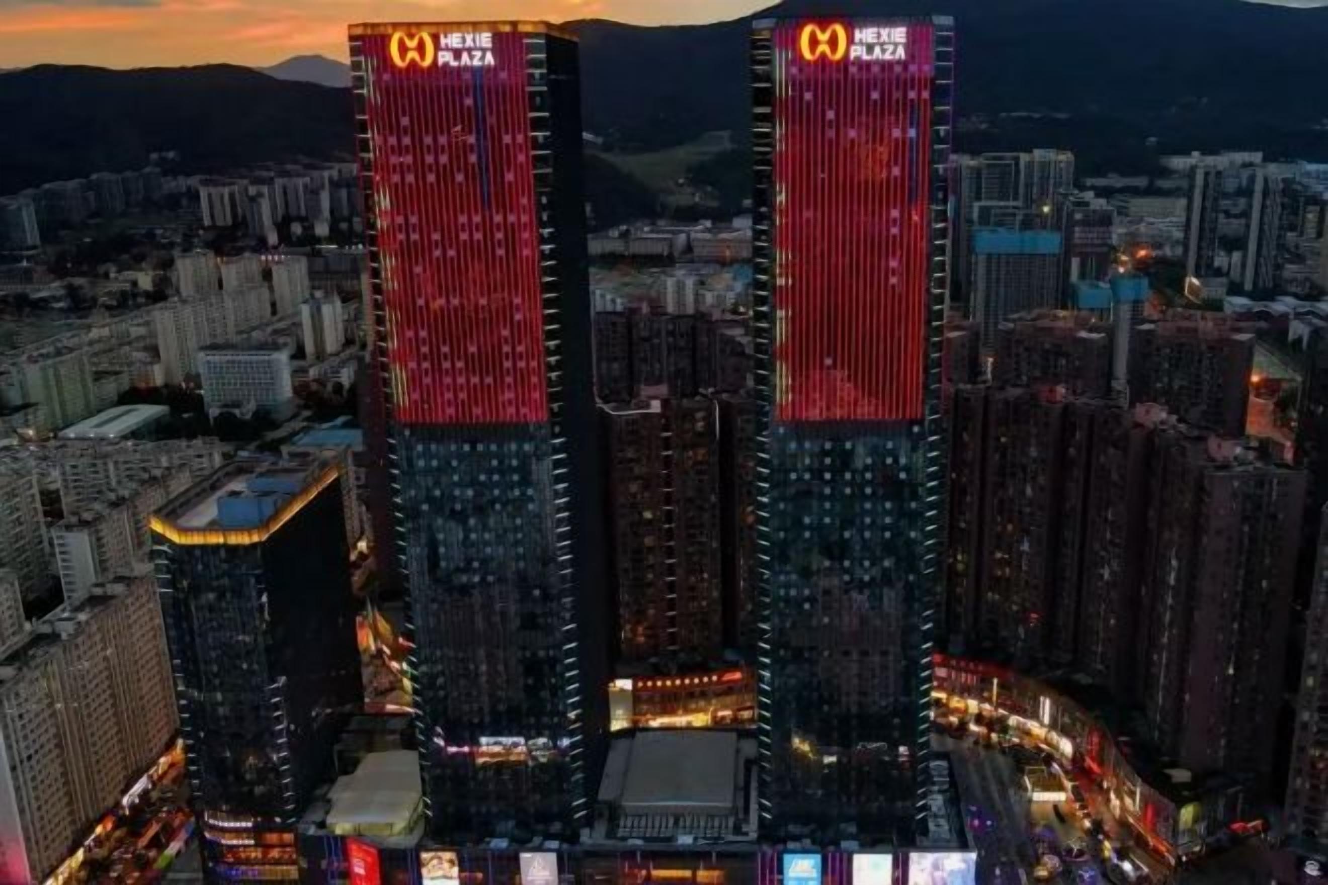 A cityscape with two prominent buildings, one with a red and white sign, and another with a similar sign.