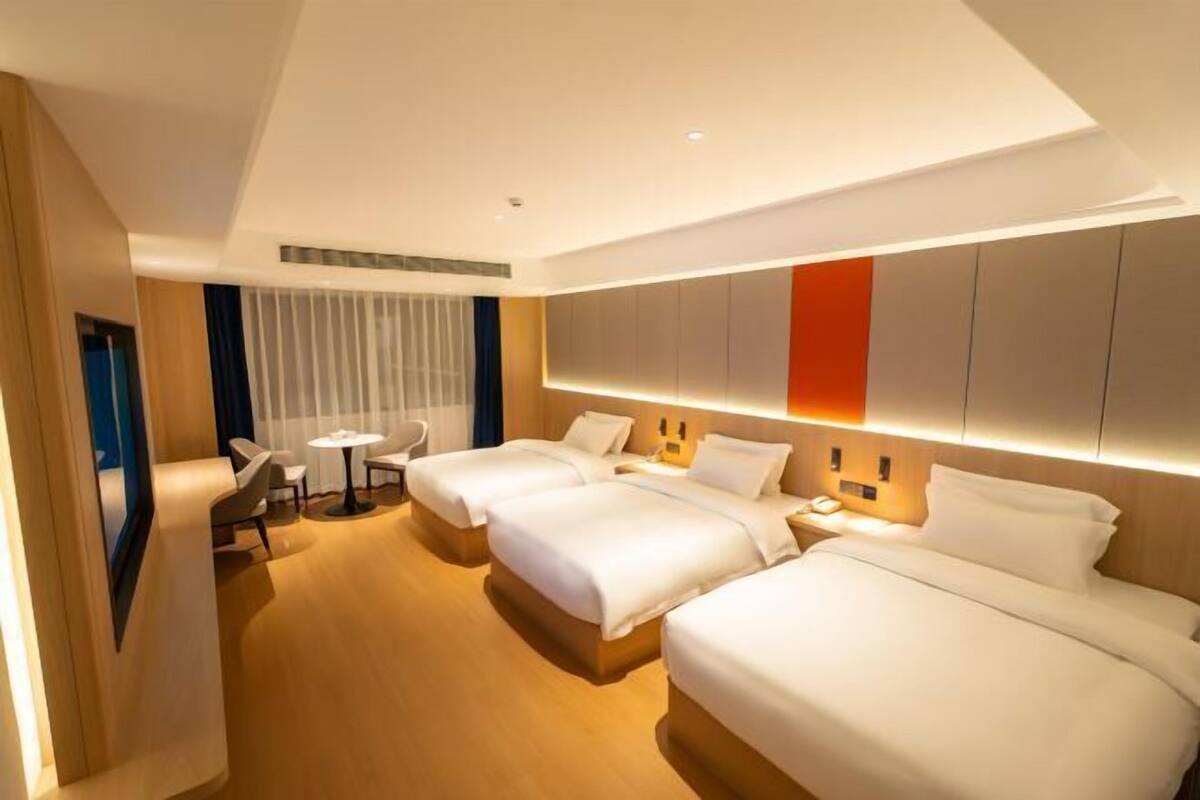 A hotel room with three beds, a desk, and a chair.