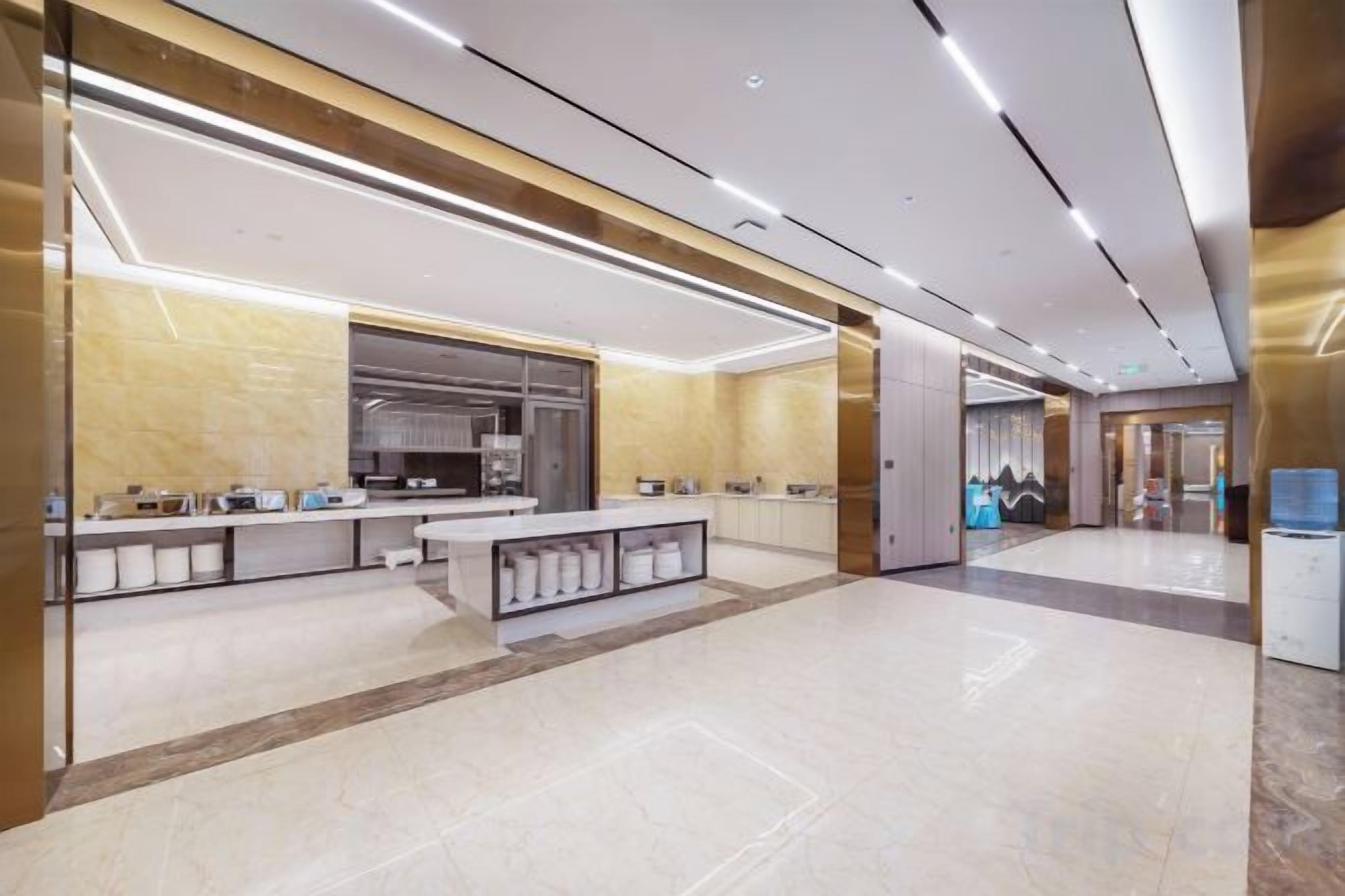 A modern hotel lobby with a central reception desk, a large kitchen area, and a spacious layout.