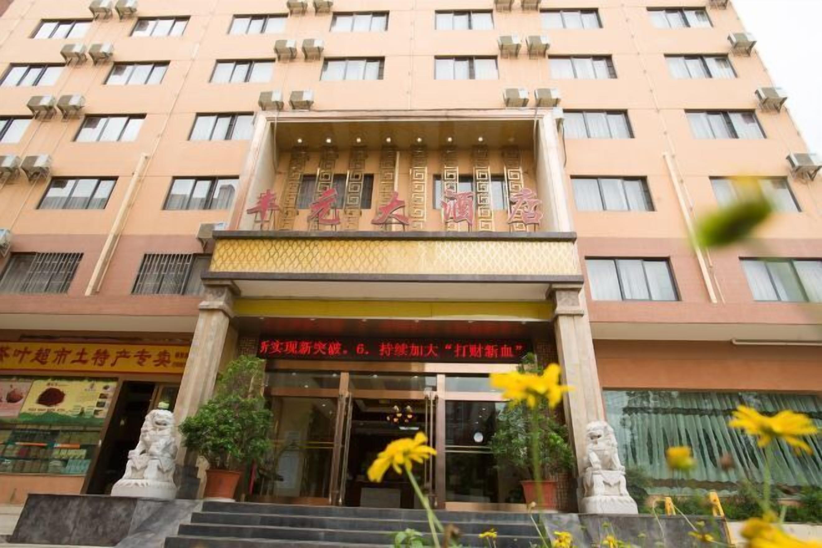 A hotel entrance with a signboard, steps leading up to the entrance, and two statues on either side.
