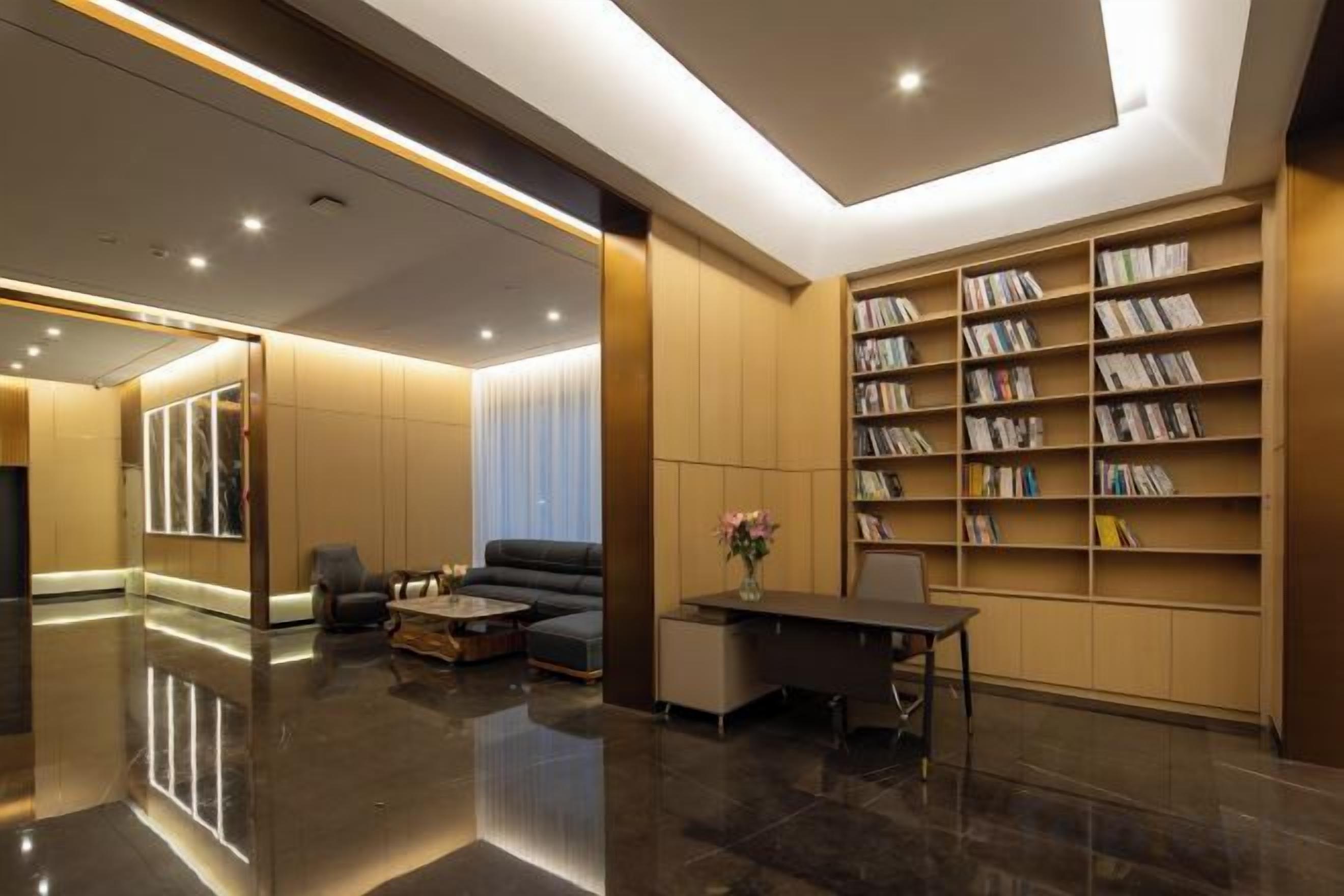Um hall moderno com piso lustroso, área de estar com sofá e mesa de centro, e uma estante repleta de livros.