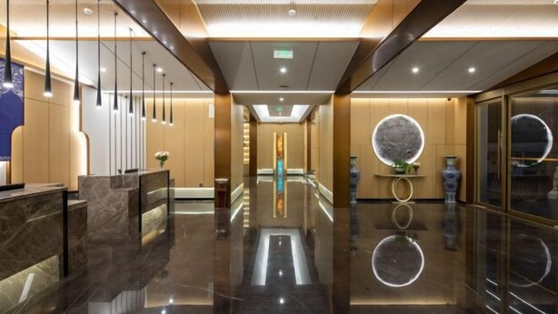 Un moderno vestíbulo de hotel con suelo reflectante, un mostrador de recepción y una lámpara central.