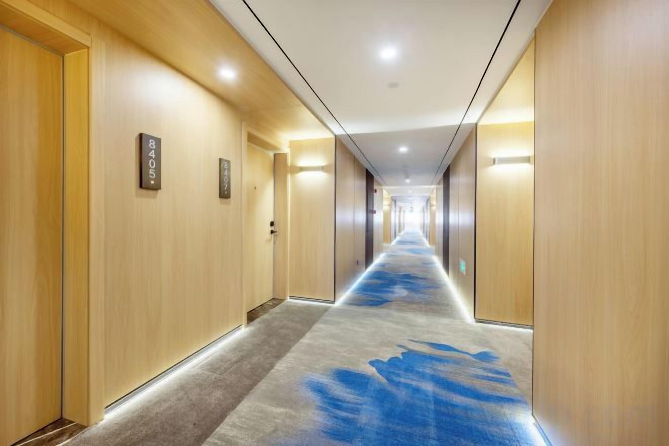 A hotel corridor with wooden walls, a carpeted floor, and doors with room numbers.