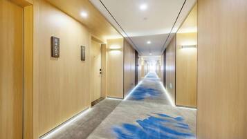 A hotel corridor with wooden walls, a carpeted floor, and doors with room numbers.