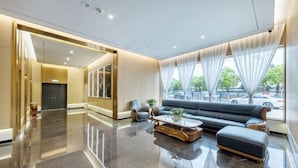 Un vestíbulo moderno con piso reflectante, un conjunto de sofás, una mesa de centro y ventanas amplias con cortinas.