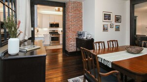 Un coin repas agrémenté d’un mur en briques apparentes, de meubles en bois et offrant une vue sur la cuisine.