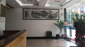 A reception area with a wooden reception desk, a framed landscape painting on the wall, and a potted plant to the right. - Tengyun Hotel (Huaiji)